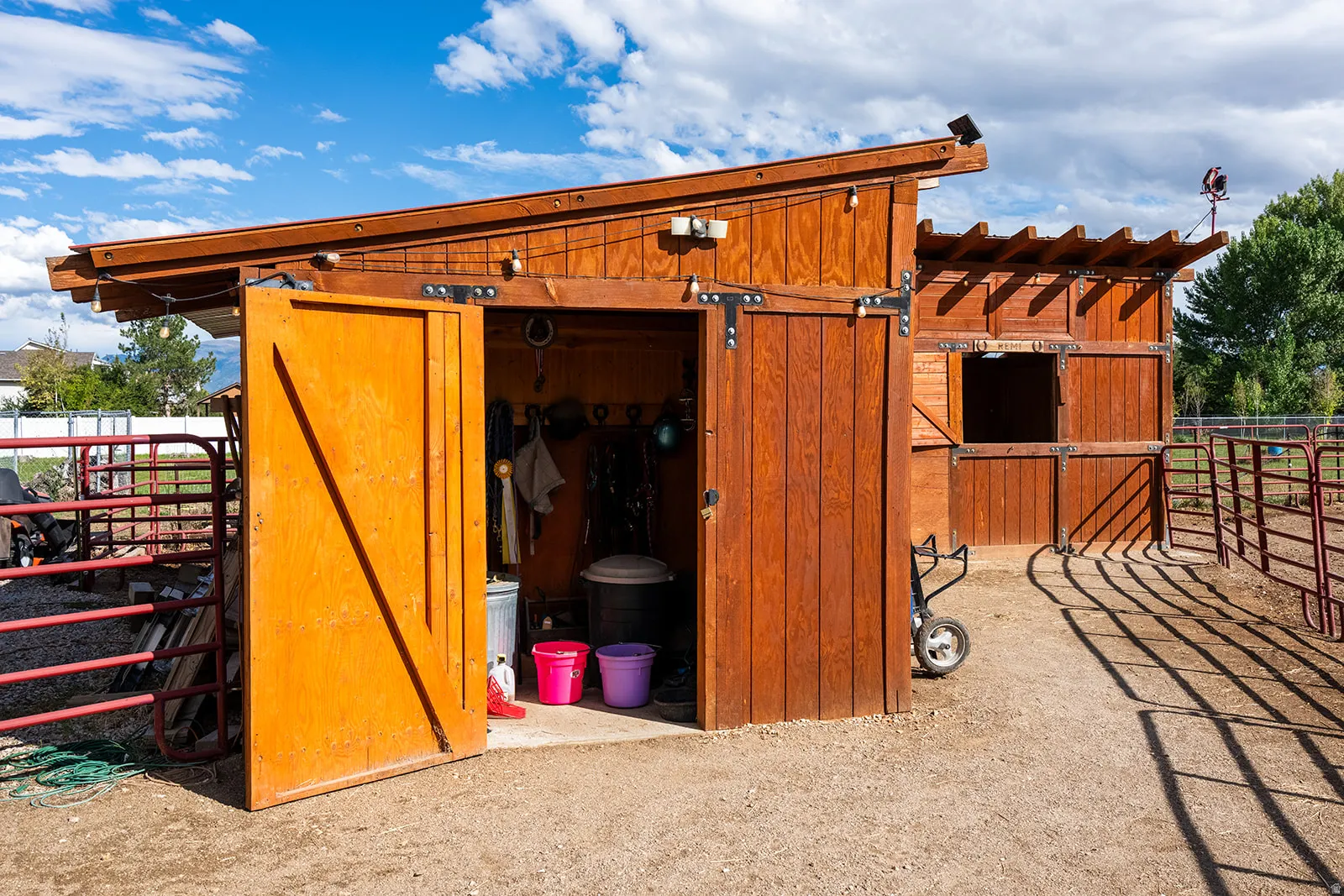 Wood-sided outbuilding featuring a sliding barn door, open stall window, and an attached slatted overhang