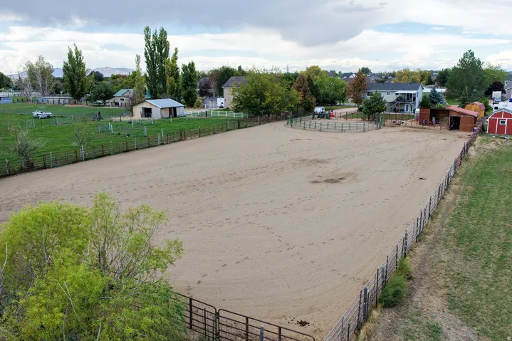 Expansive outdoor arena with sand footing, enclosed by fencing, featuring a round pen and a red barn structure