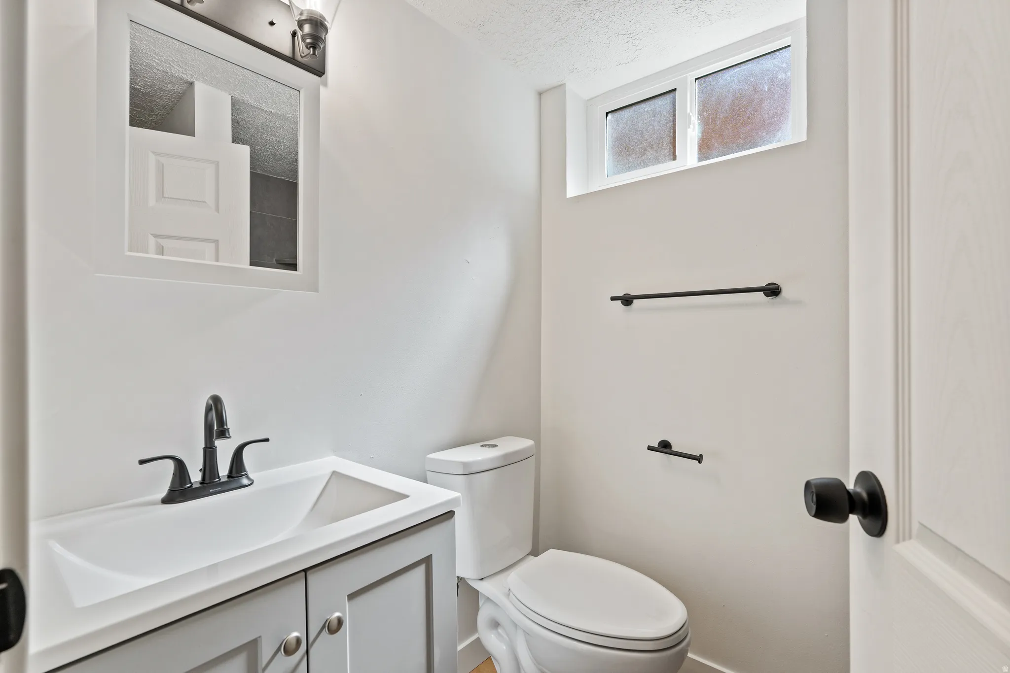 Bathroom featuring a gray vanity with integrated sink, matte black faucet, wall-mounted medicine cabinet, modern toilet, and a frosted transom window