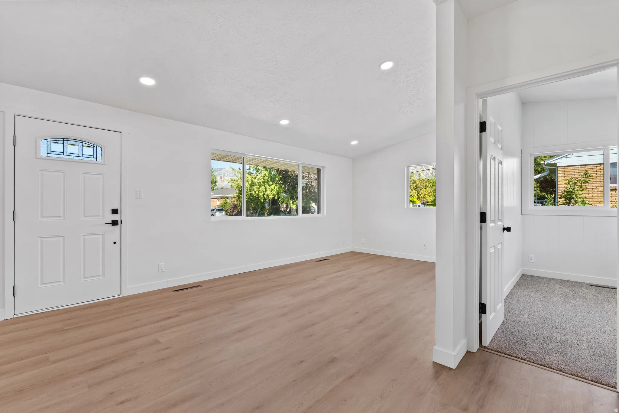 Recessed lighting, wood-finish flooring, white paneled door with decorative glass, white walls, and multiple windows