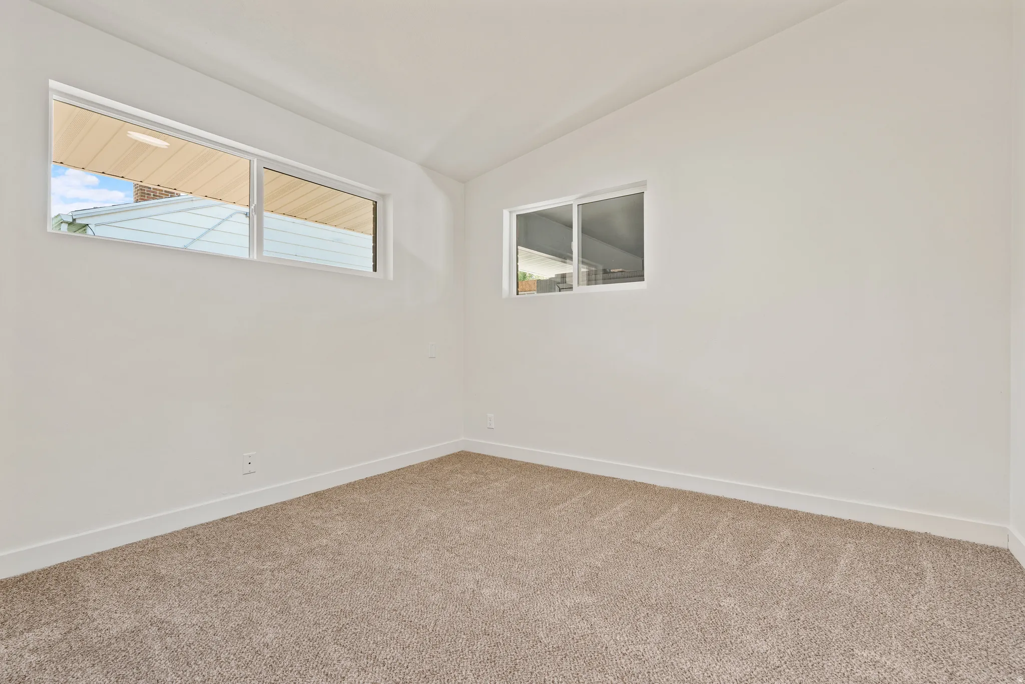 Recessed windows on two walls, vaulted ceiling, and neutral carpet flooring