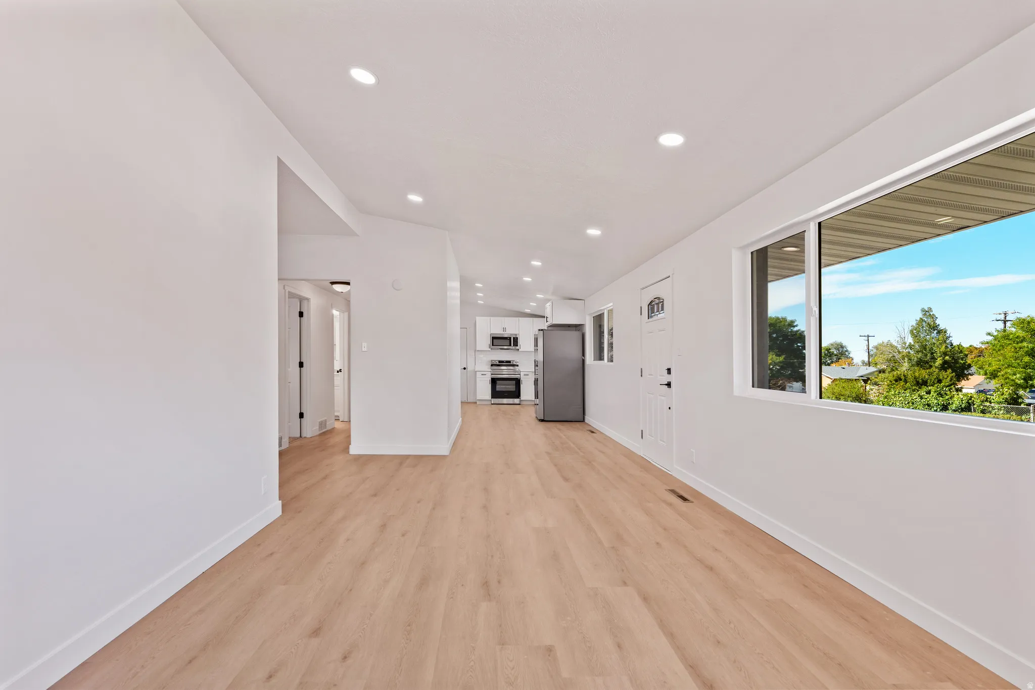 Open-concept living area with wood-finish flooring, white walls, recessed lighting, and a large window