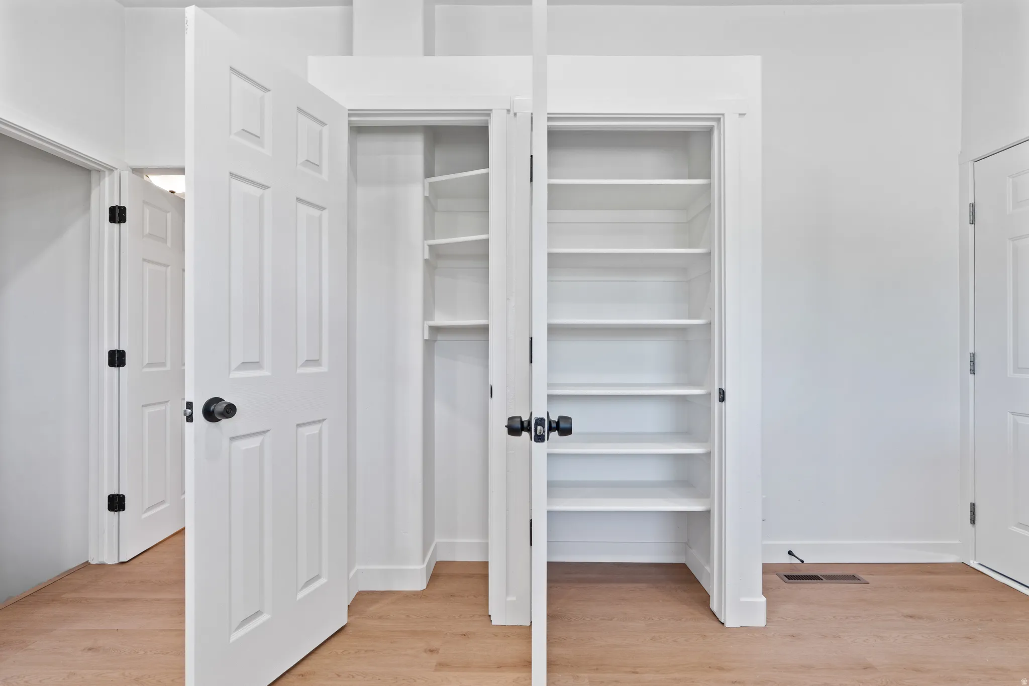 Built-in shelving, wood-finish flooring, white paneled doors, and matte black hardware