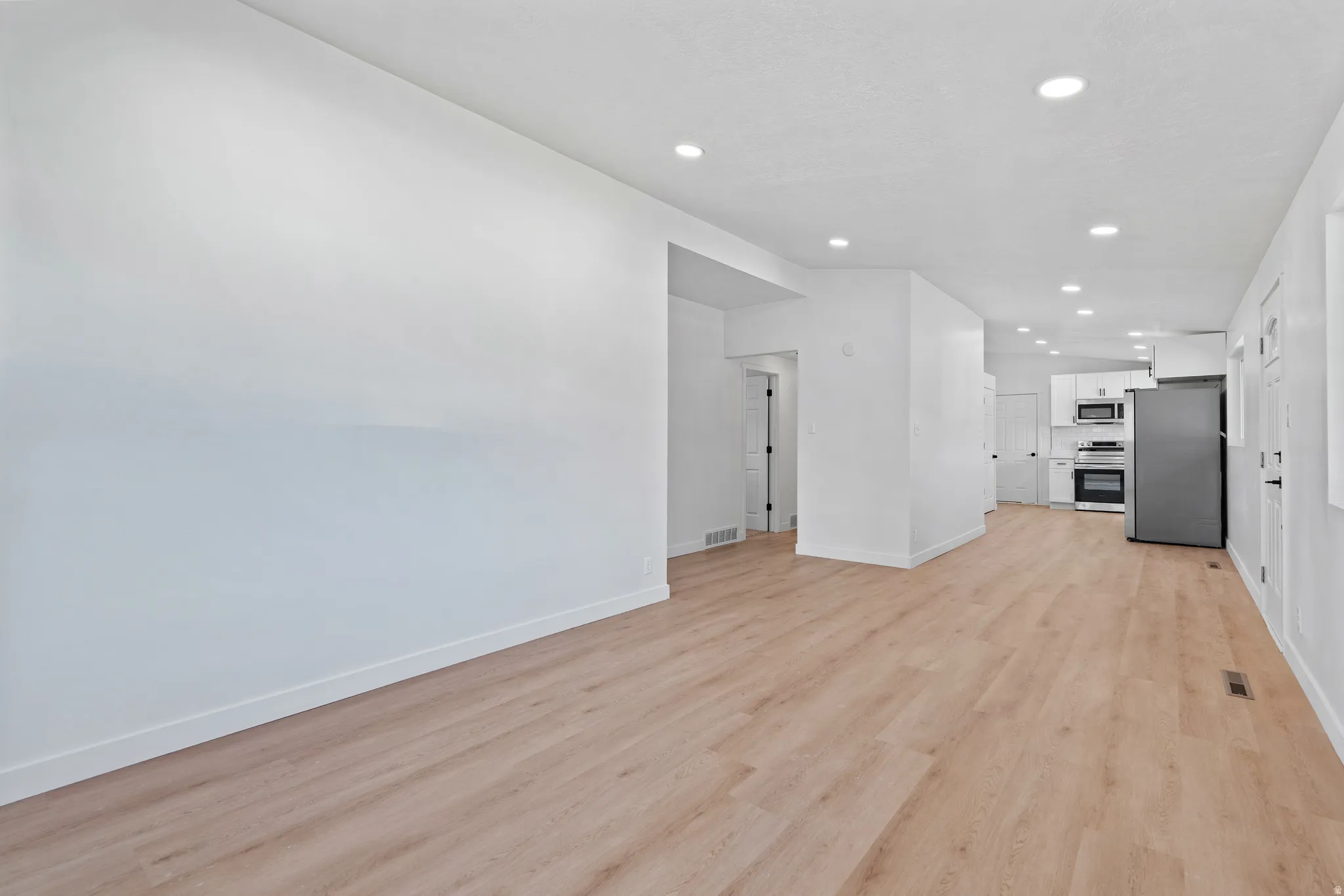 Open-concept living area with wood-finish flooring, recessed lighting, and a kitchen featuring stainless steel appliances and white cabinetry