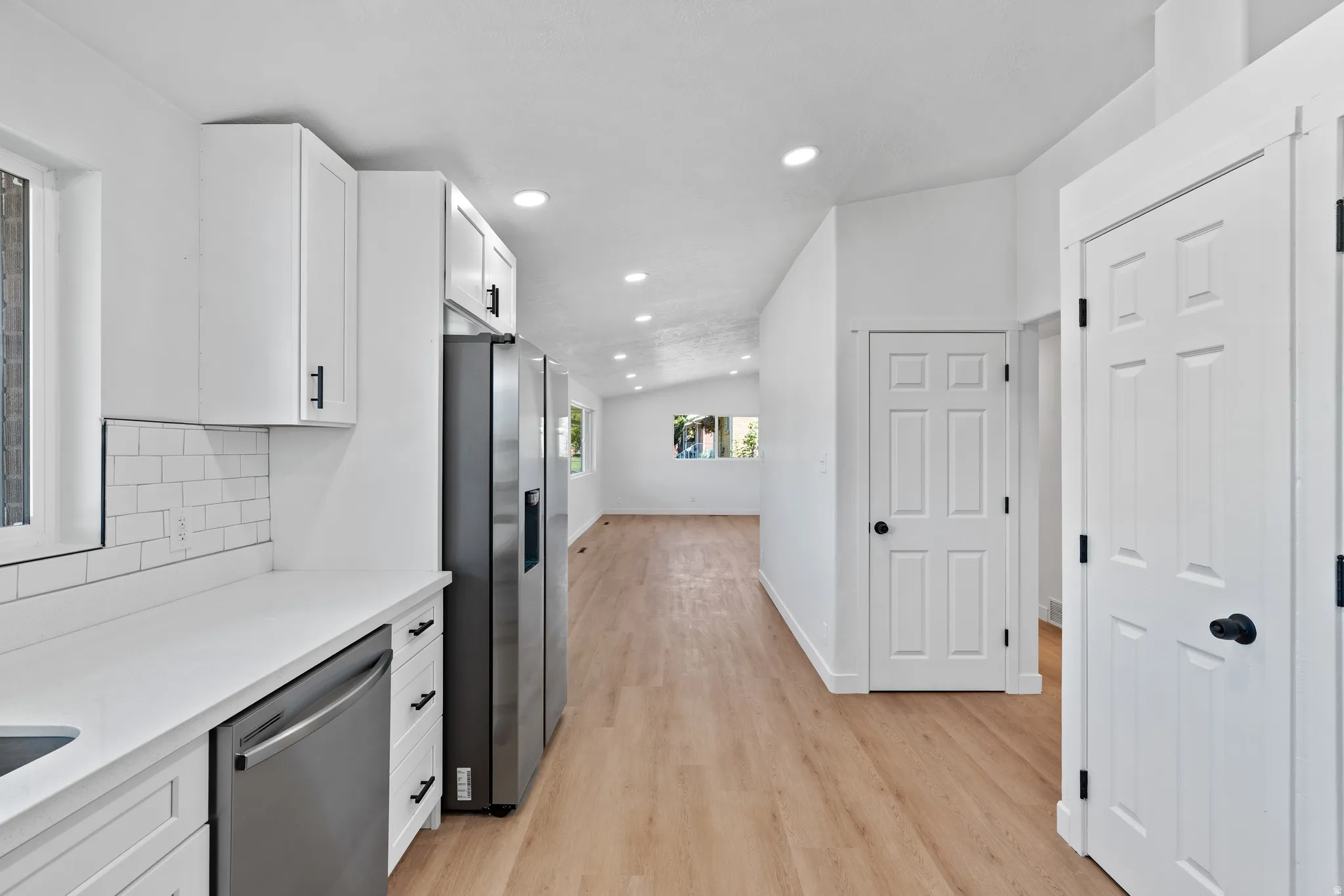 Kitchen with white cabinetry, stainless steel appliances, white subway tile backsplash, and light wood-finish flooring