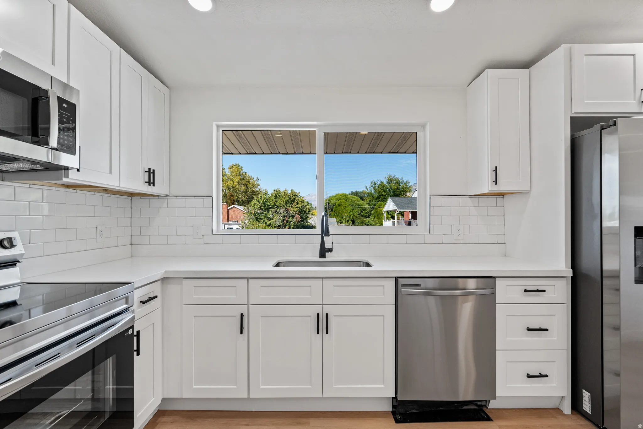 White shaker-style cabinetry with matte black hardware, stainless steel appliances, white subway tile backsplash, white countertops, and wood-finish flooring