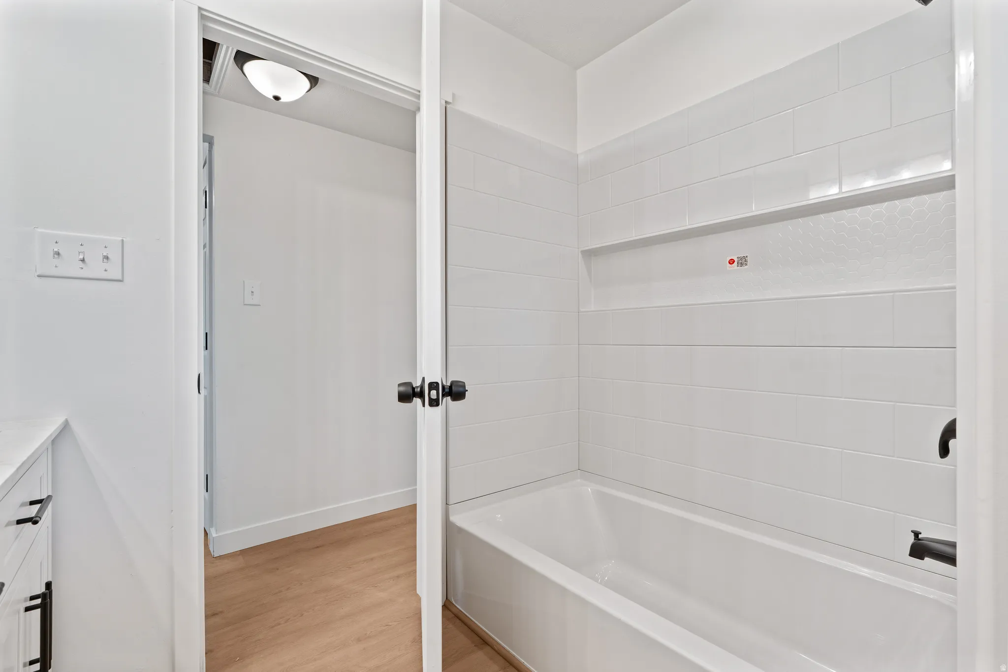 Bathtub with white subway tile surround, built-in shelf, and matte black fixtures