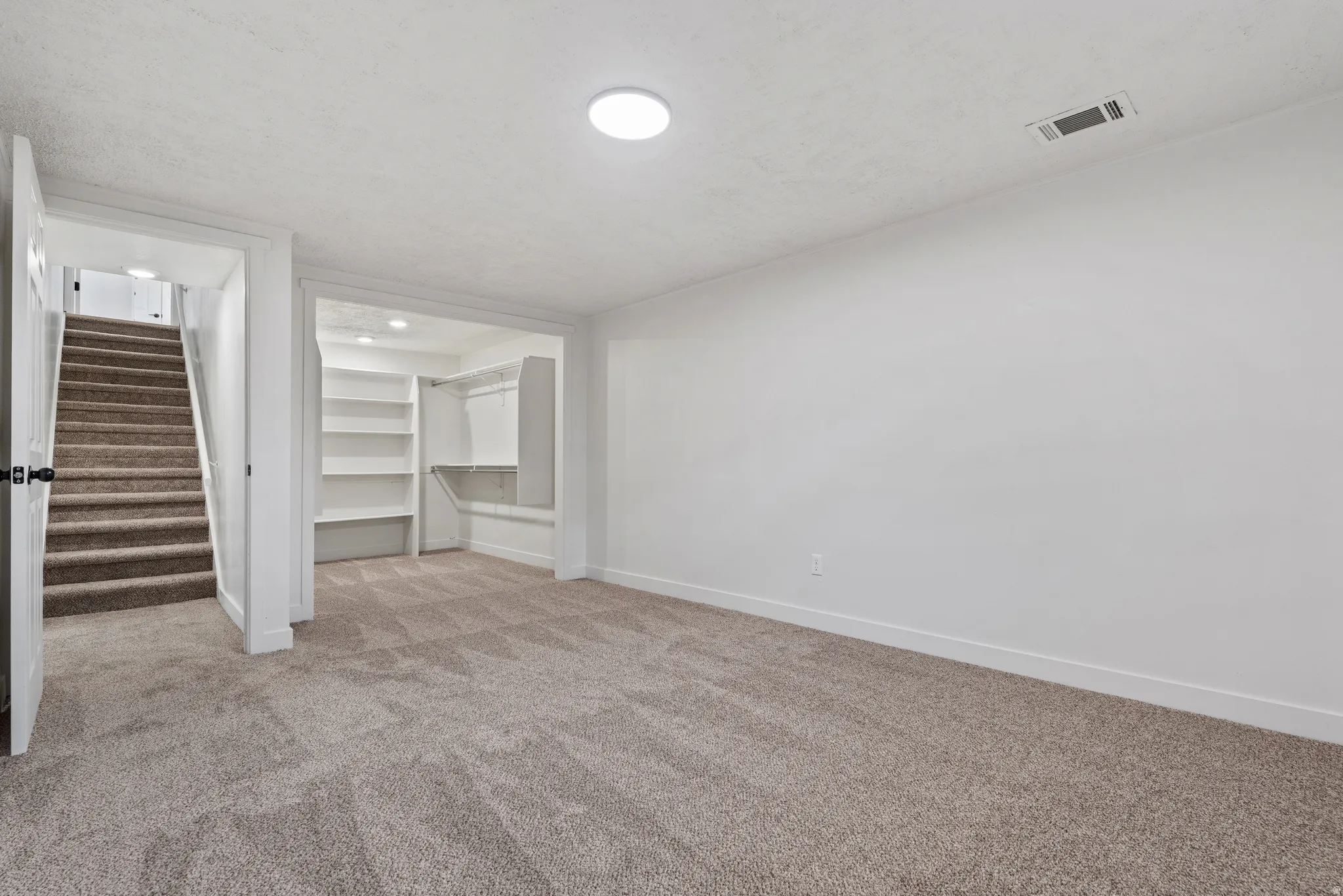 Carpeted flooring, white walls, built-in shelving, recessed lighting, and a circular ceiling light fixture