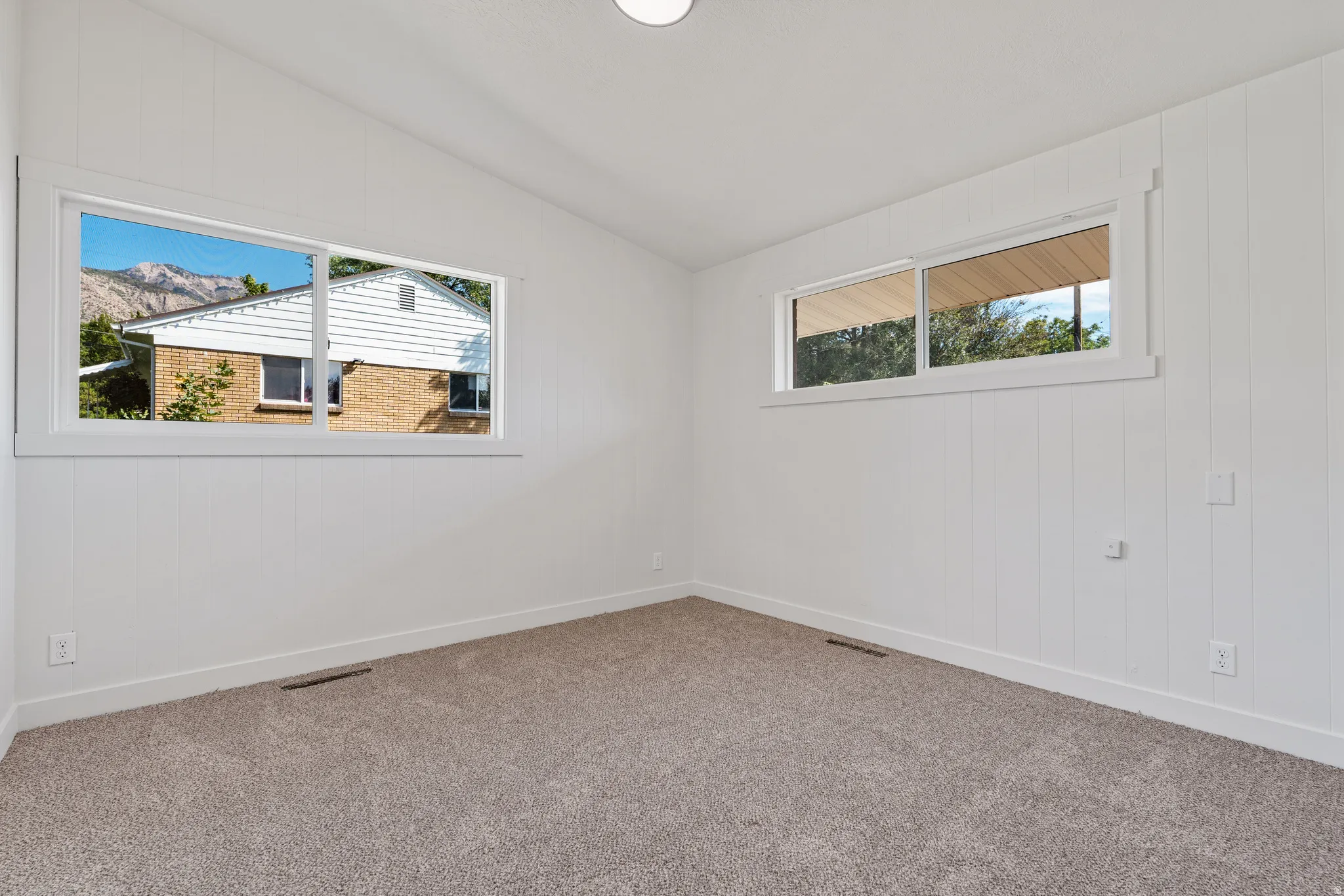 Light gray carpeted flooring, white paneled walls, and two large windows with white trim