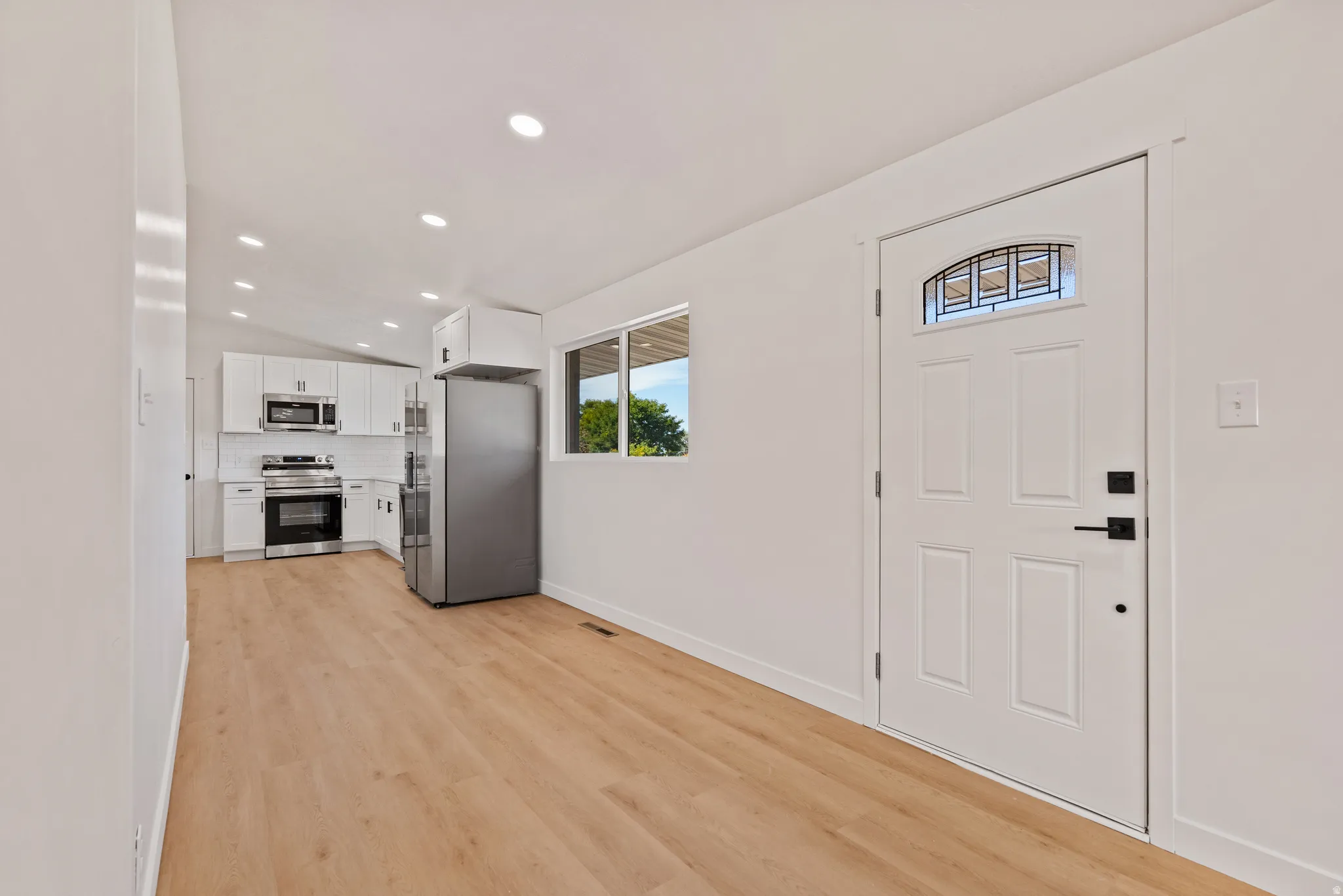 Open-concept living space with wood-finish flooring, recessed lighting, and a white paneled entry door