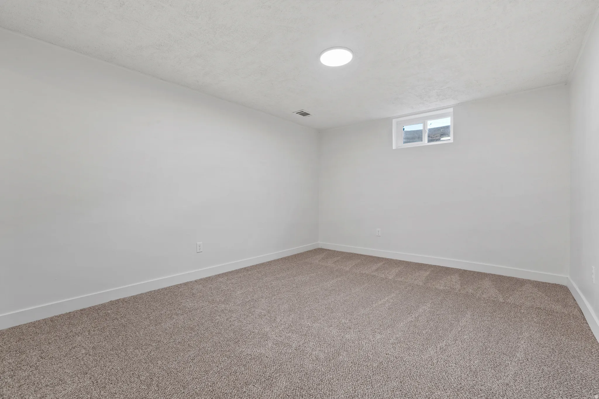 Neutral-toned carpet flooring, white painted walls, window for natural light, circular overhead light fixture