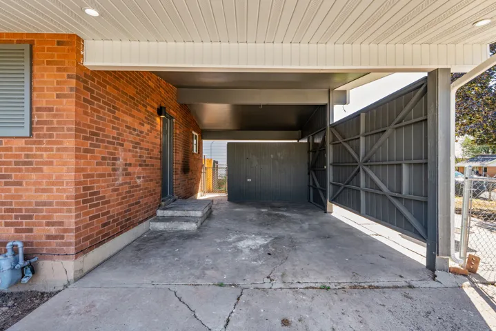 Covered carport with a concrete surface, brick exterior wall, and integrated lighting
