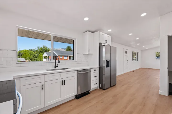 Kitchen featuring white shaker cabinetry, stainless steel appliances, a white subway tile backsplash, and light wood-finish flooring