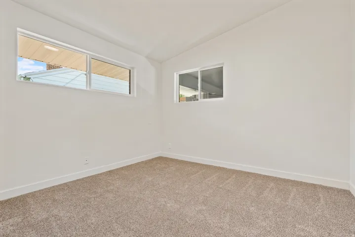 Recessed windows on two walls, vaulted ceiling, and neutral carpet flooring