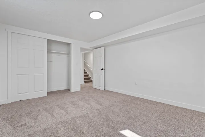 Neutral carpeting, white painted walls, white trim, recessed lighting, and a closet with bi-fold doors