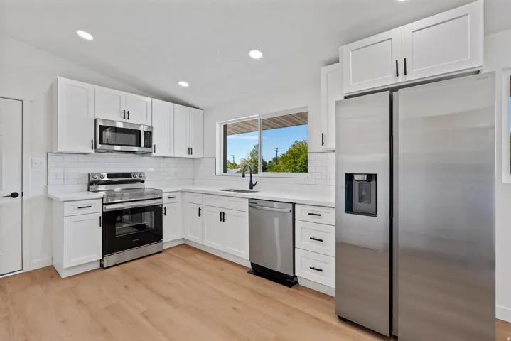 Kitchen featuring white cabinetry, stainless steel appliances, white subway tile backsplash, and light wood-finish flooring