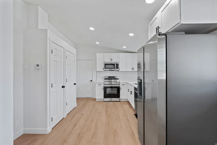 Kitchen featuring stainless steel appliances, white cabinetry with dark hardware, wood-finish flooring, a white subway tile backsplash, and recessed lighting