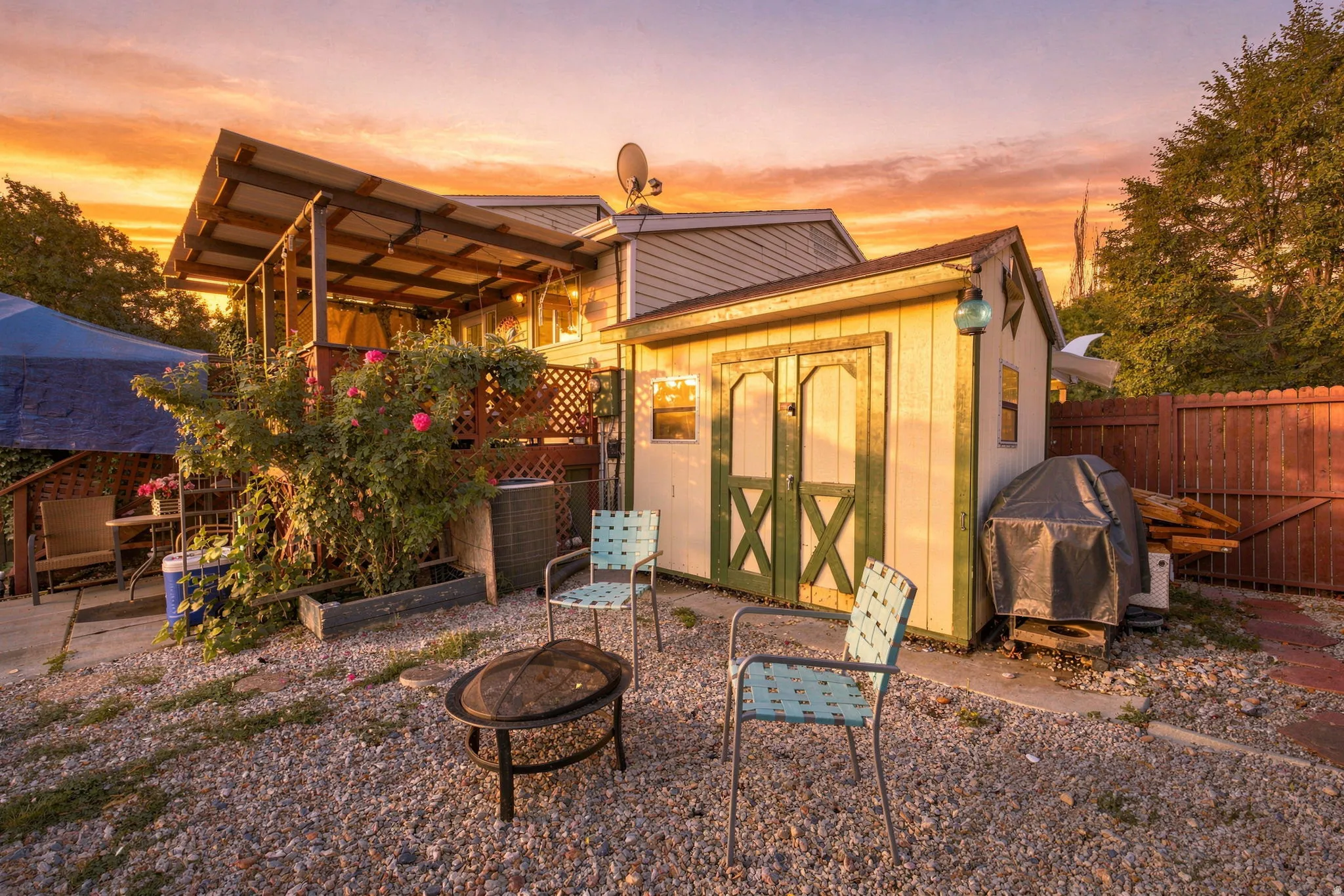 Gravel outdoor area with a built-in fire pit, covered patio structure, and a storage shed