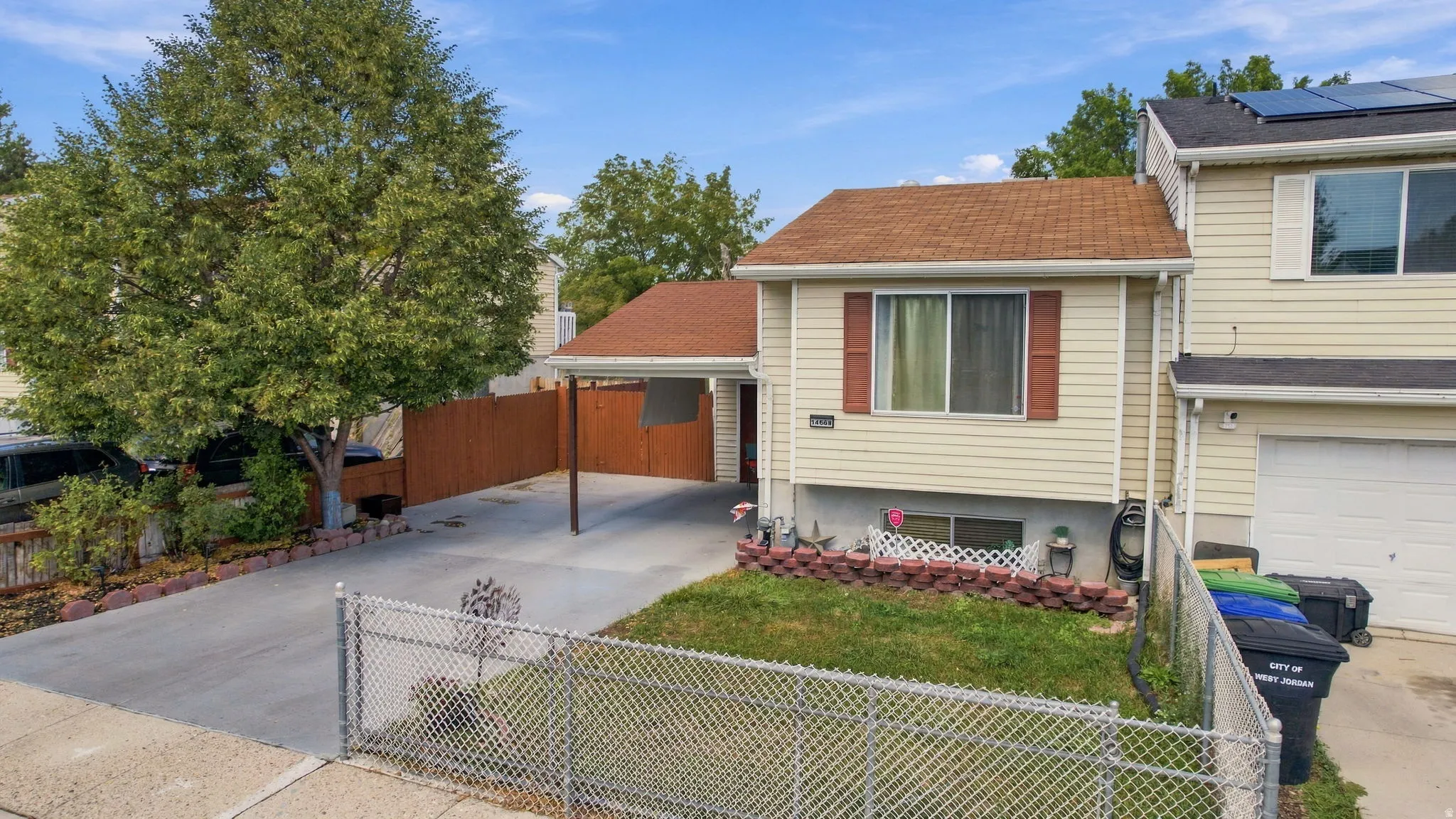 Siding exterior with a carport, established tree, and fenced front yard