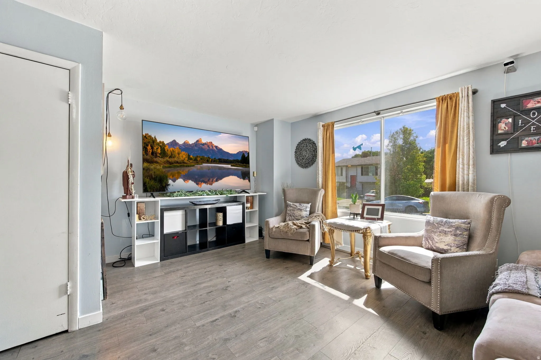 Wood-finish flooring, white trim, light blue wall paint, and large windows with natural light