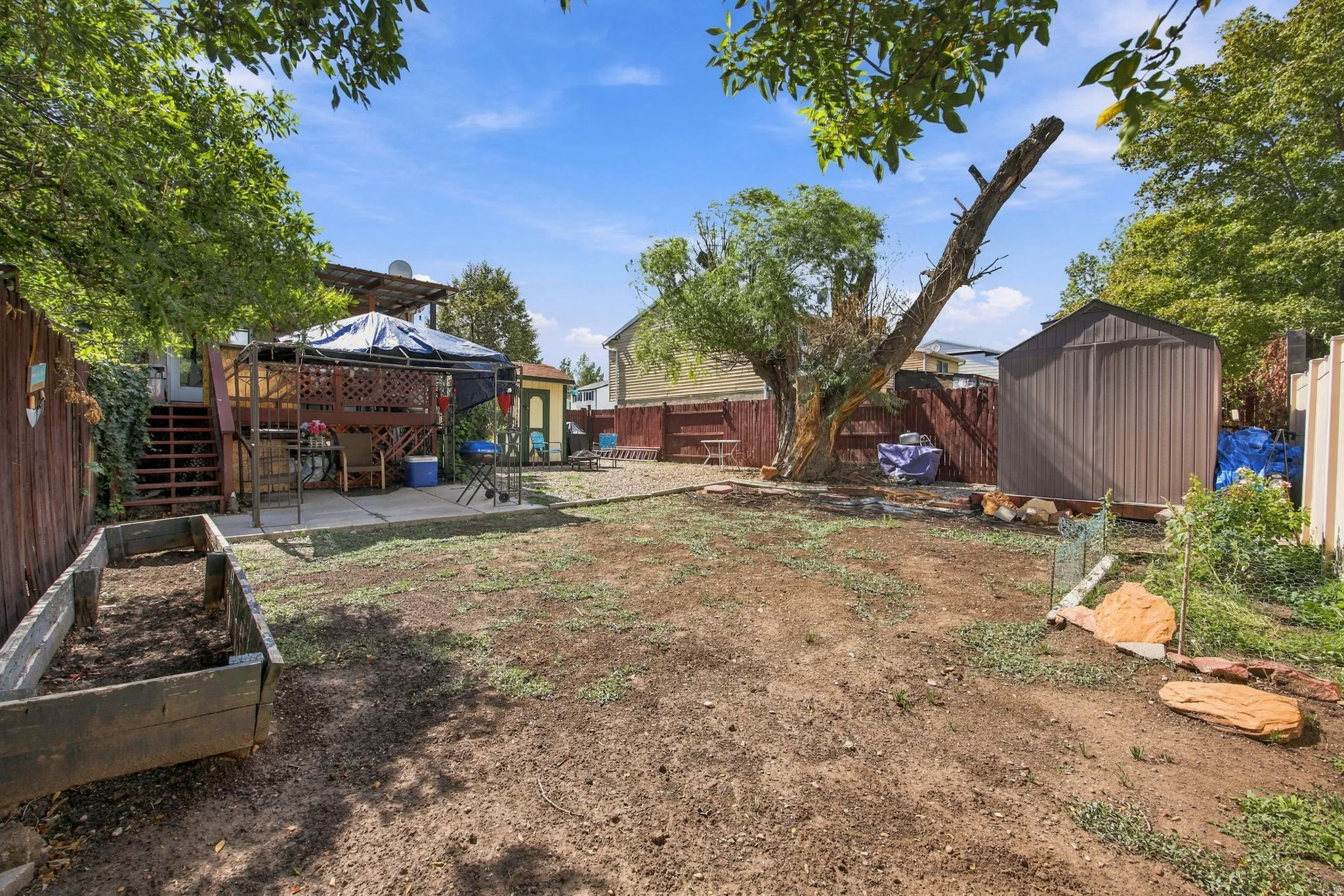 Expansive backyard featuring a concrete patio, wood deck with lattice railing, a raised garden bed, and a metal storage shed