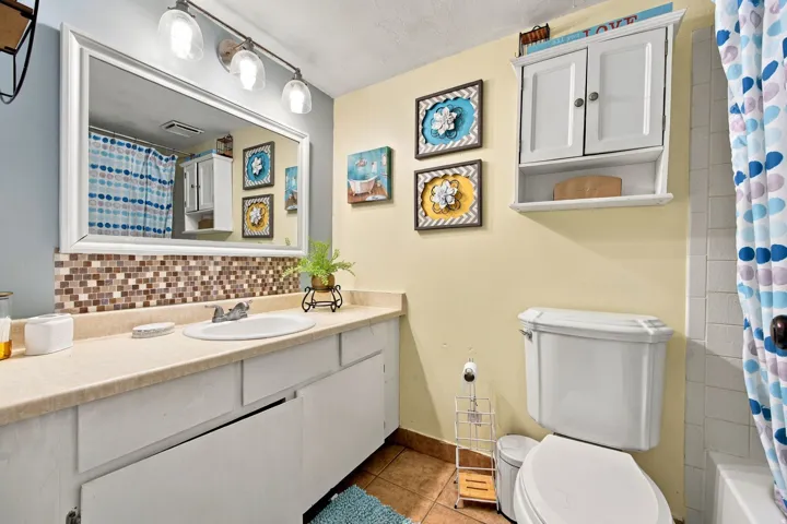 Vanity with an integrated sink, mosaic tile backsplash, and a framed mirror with overhead lighting