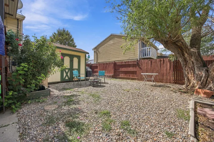 Gravel-covered yard with a large mature tree, wood fencing, and a detached storage shed