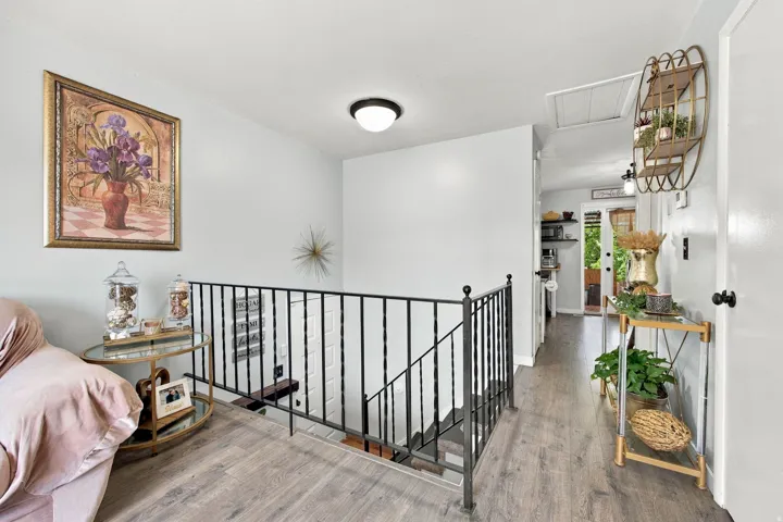 Wood-finish flooring throughout, wrought iron railing, contemporary ceiling light fixture, and a built-in wall shelf