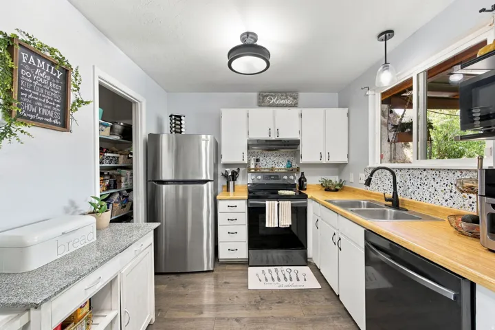 Kitchen featuring wood-finish flooring, white cabinetry, a double basin sink with a matte black faucet, light wood-finish countertops, and a built-in pantry