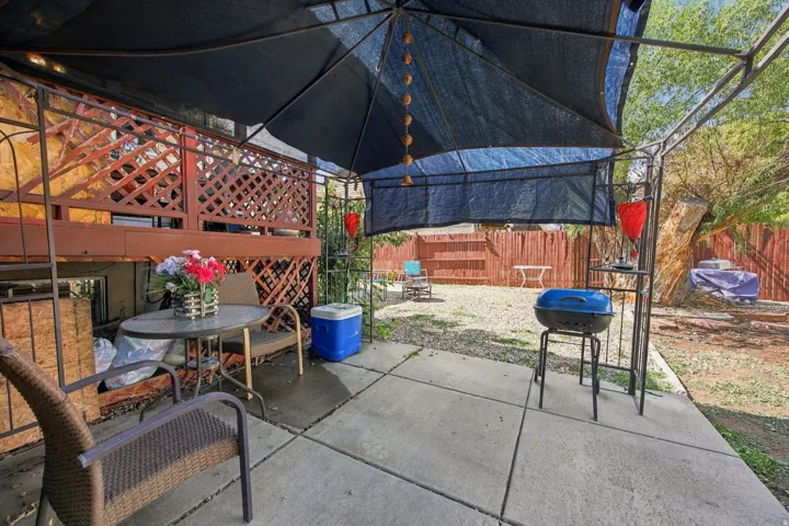 Rear patio with concrete slab flooring, metal-framed overhead sunshade, and a raised wood deck featuring lattice railing