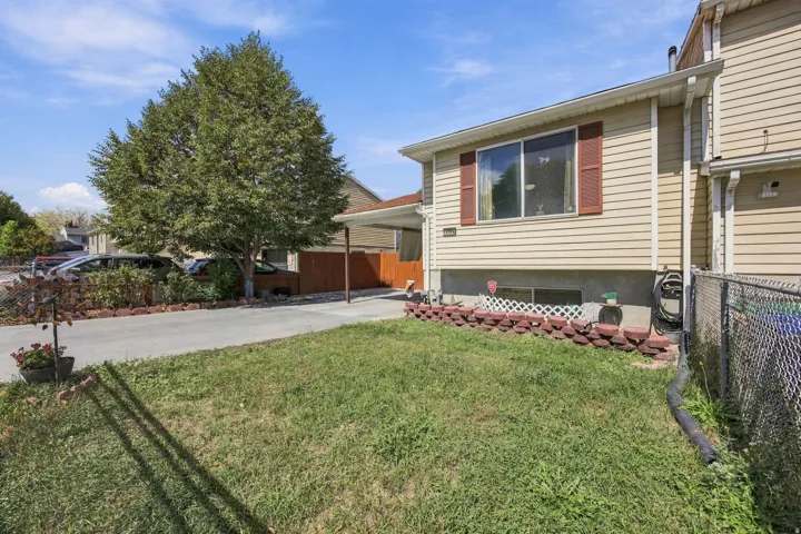 Cream-colored siding exterior, red window shutters, concrete driveway, attached carport, and mature tree