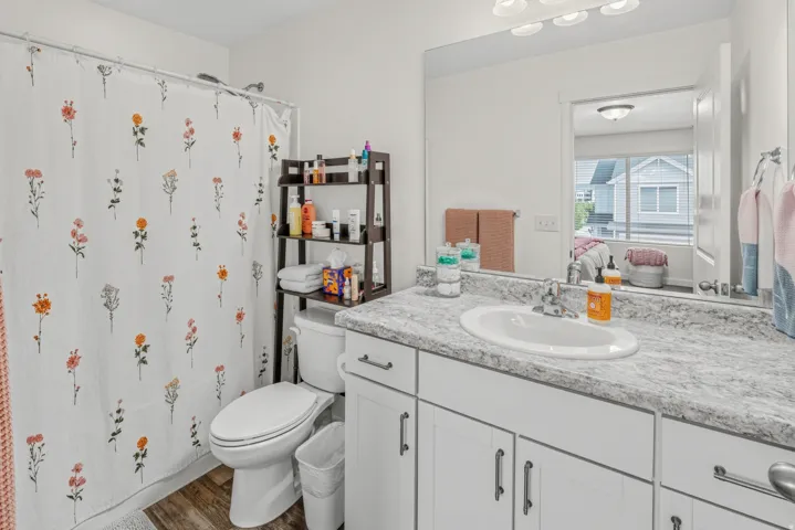 Wood-finish flooring, white vanity with integrated sink, white countertop, white toilet, and fixed wall mirror