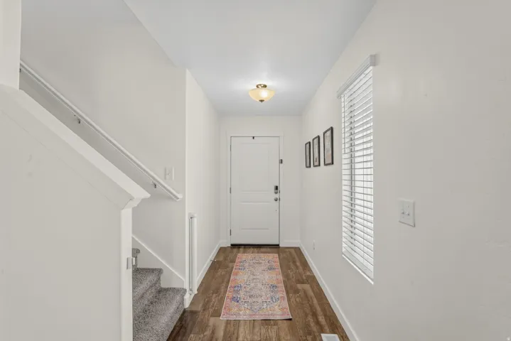Wood-finish flooring, staircase with carpeted treads, window with blinds, and flush-mount ceiling light fixture