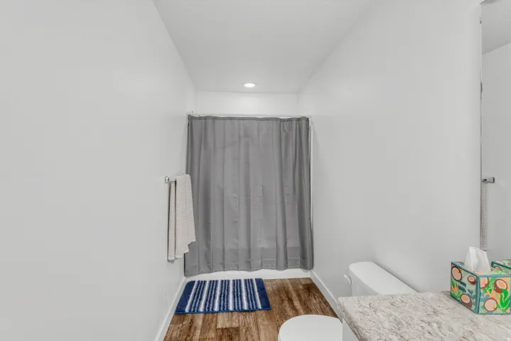 White walls with recessed lighting, wood-finish flooring, a shower area with a gray curtain, and a vanity with a light-colored countertop