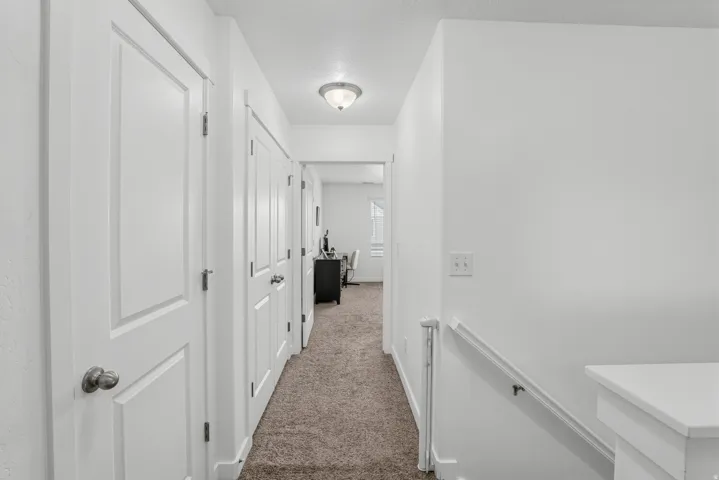 Hallway with white walls, carpeted flooring, and a flush-mount ceiling light