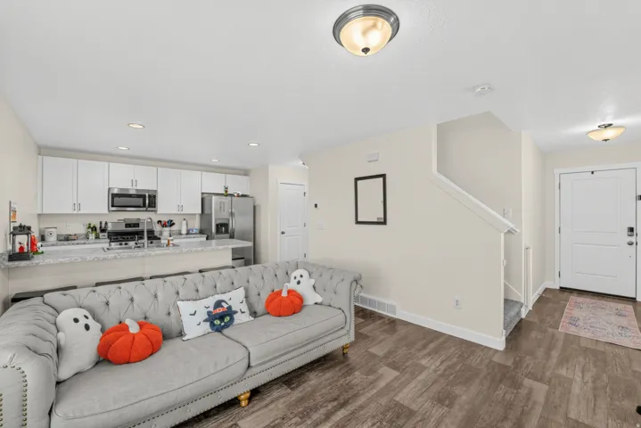 Open-concept living space featuring wood-finish flooring, recessed lighting, white kitchen cabinetry, stainless steel appliances, and a staircase with carpeting