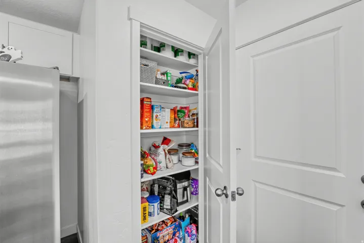 Built-in pantry with multiple white shelves, white trim, and a white panel door