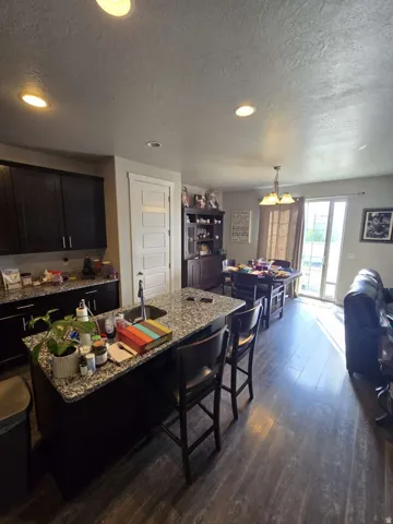 Kitchen featuring dark wood cabinetry, granite countertops, wood-finish flooring, recessed lighting, and a kitchen island with an integrated sink