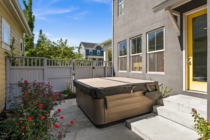 Private patio space featuring a hot tub, stucco exterior, multiple windows, and a vibrant yellow entry door