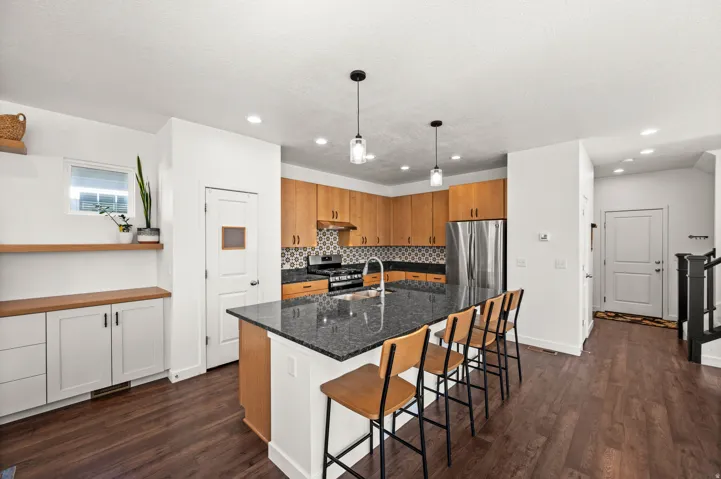 Open-concept kitchen featuring an oversized island with seating, dark stone countertops, wood cabinetry, and a patterned tile backsplash