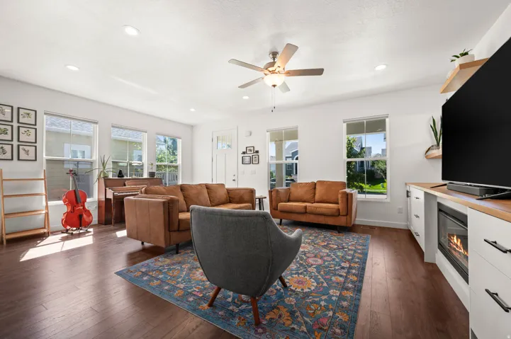Recessed lighting illuminates the open living area featuring wood-finish flooring, multiple windows, and a ceiling fan