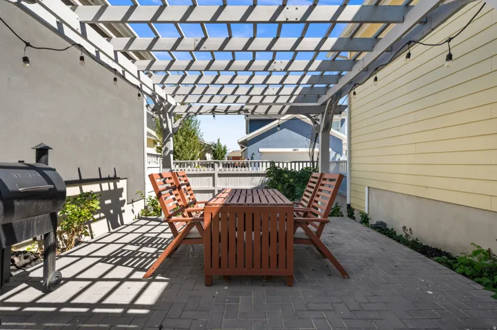 Paved patio area featuring a slatted pergola structure and string lighting