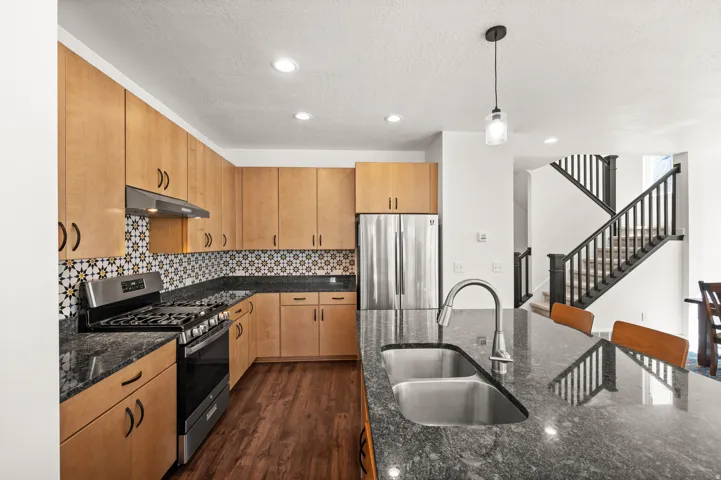 Kitchen featuring wood-finish cabinetry, patterned tile backsplash, stainless steel appliances, and granite countertops with a dual basin sink