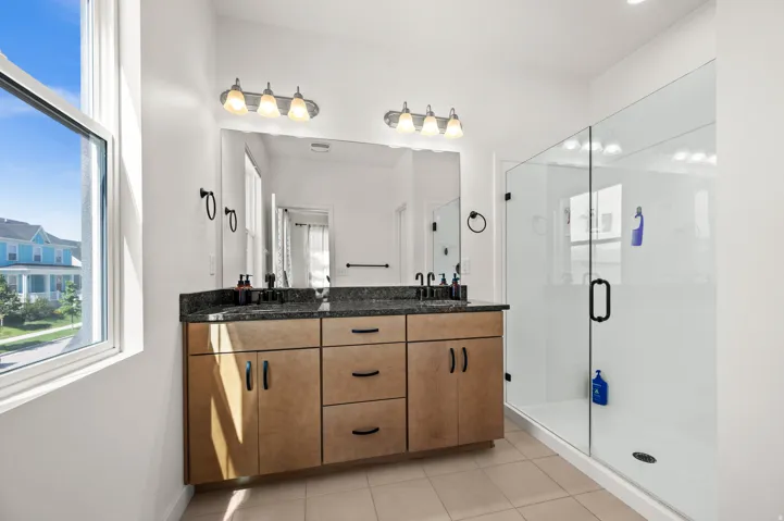 Dual vanity with dark stone countertop, undermount sinks, and wood-finish cabinetry