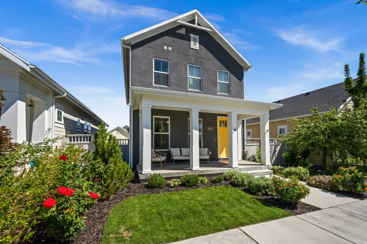 Stucco exterior with white trim, covered front porch, vibrant yellow entry door, concrete pathway, and mature landscaping