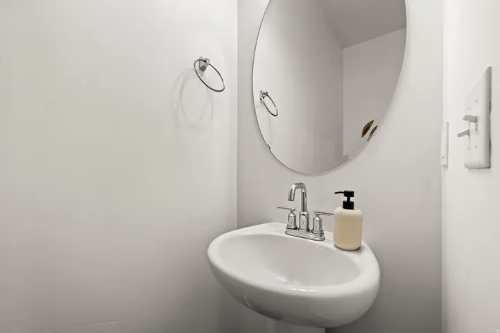 Pedestal sink with a chrome faucet, oval mirror, and towel ring