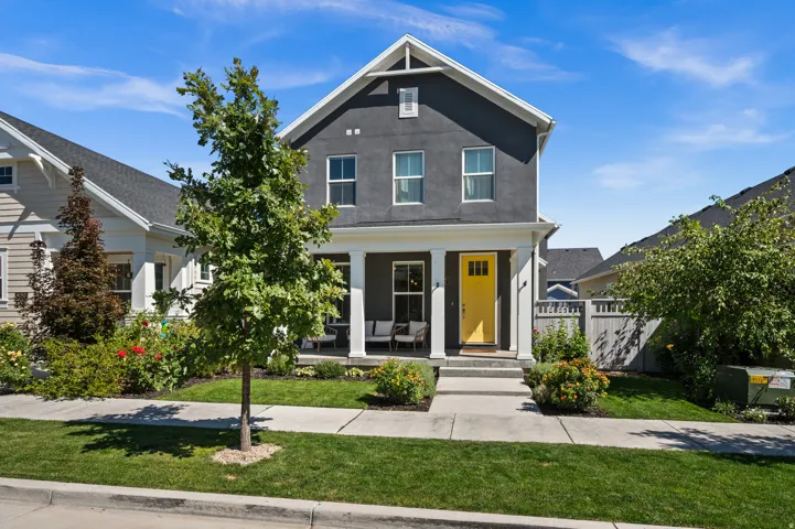 Two-story home with a prominent porch, vibrant yellow front door, and a manicured lawn featuring mature landscaping