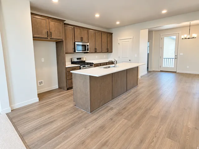 Open-concept kitchen with wood-finish flooring, stainless steel appliances, a center island with an undermount sink, and recessed lighting