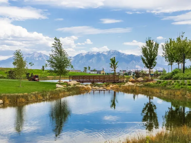Manicured greenspace with a serene pond, pedestrian bridge, and distant mountain backdrop