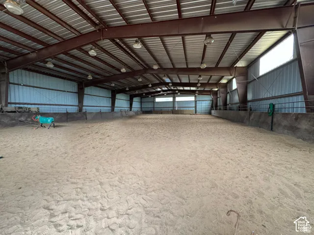 Spacious indoor arena featuring a sand surface, metal frame construction, corrugated metal walls, and overhead lighting